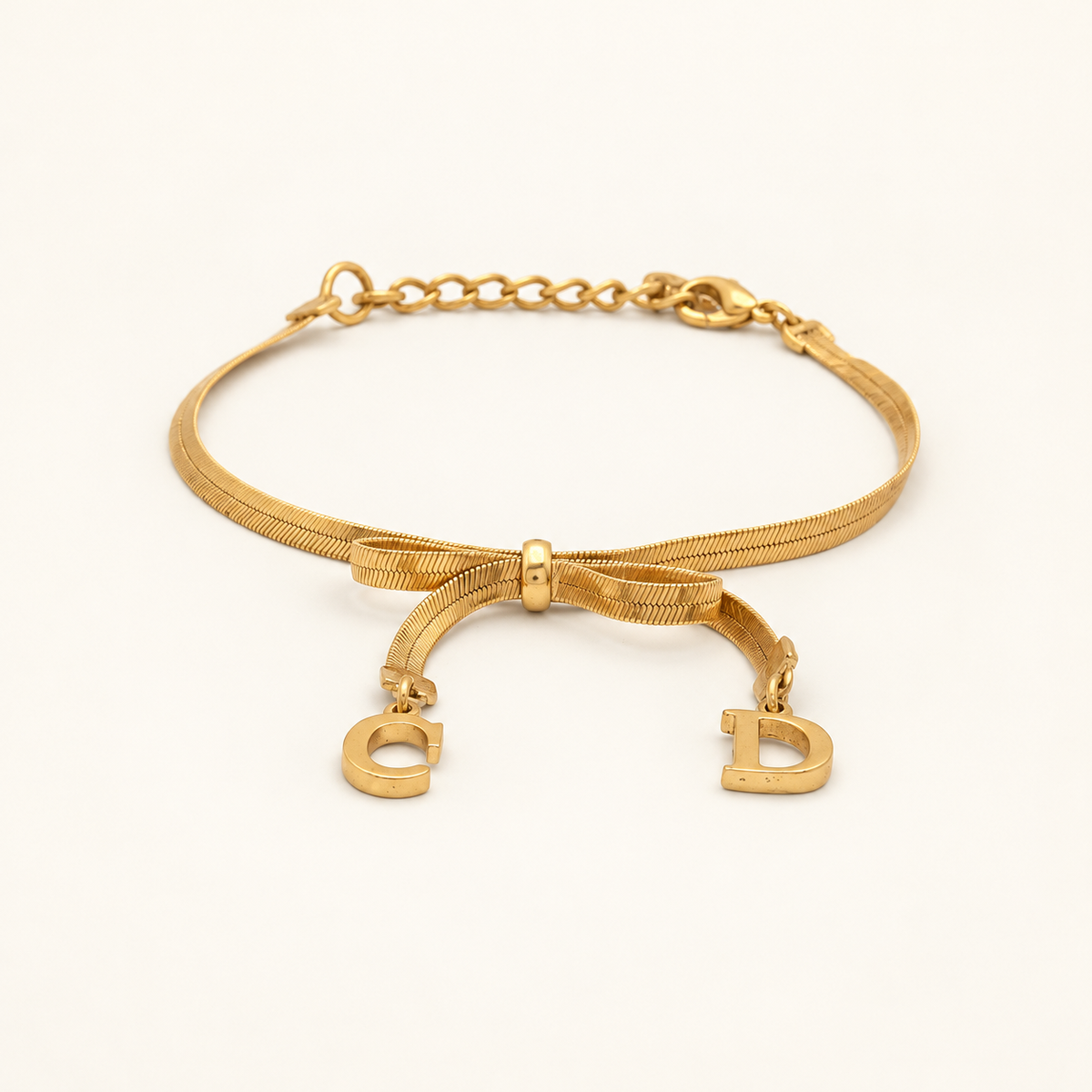 Christian Dior Gold-Tone Bow CD Charm Bracelet, 19cm — front view on an ivory background