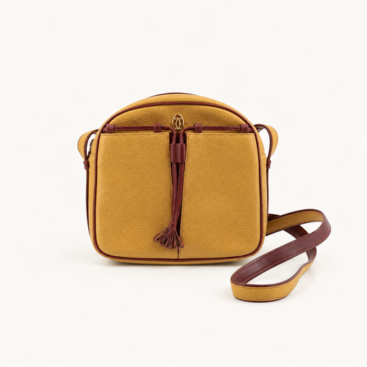 Front view of a mustard yellow Cartier Must de Cartier shoulder bag with burgundy trim, tassel and long shoulder strap
